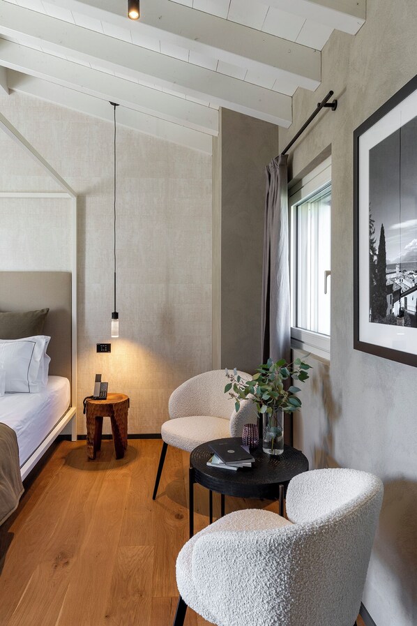 Een moderne hotelkamer met een bed, een zithoek met stoelen, een klein tafeltje en een aan de muur hangend schilderij.
