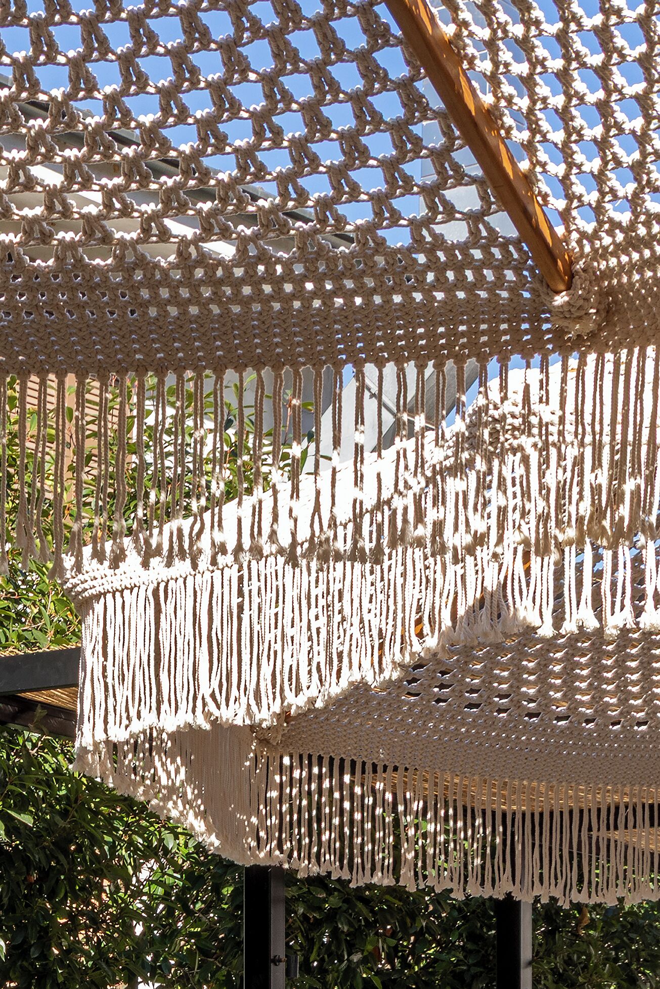 Un dosel de macramé con estructura de madera y flecos colgantes, que proporciona sombra.