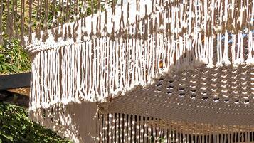 Un dosel de macramé con estructura de madera y flecos colgantes, que proporciona sombra.