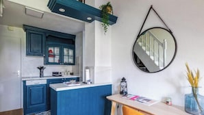 A compact kitchen with blue cabinets, a white countertop, and a round mirror on the wall.