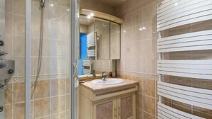 A bathroom with a glass shower enclosure, a sink with a mirror above it, and a towel rack with horizontal bars.