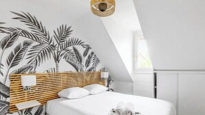 A bedroom with a slatted wooden headboard, white bedding, and a tropical leaf wallpaper.