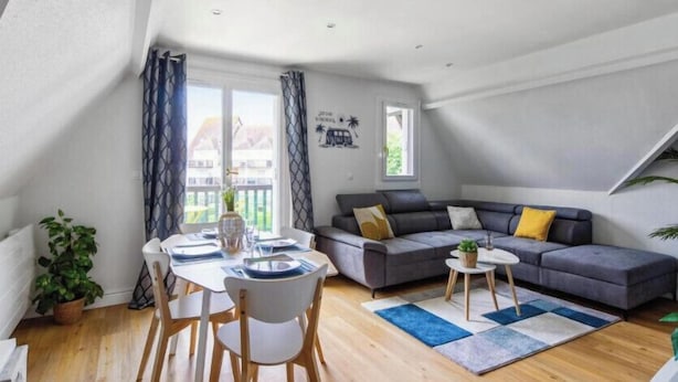 A modern loft apartment with a dining area, a gray sofa, and a large window with curtains.
