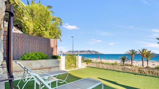 A patio with two white lounge chairs, a stone wall, and a view of the beach and ocean.
