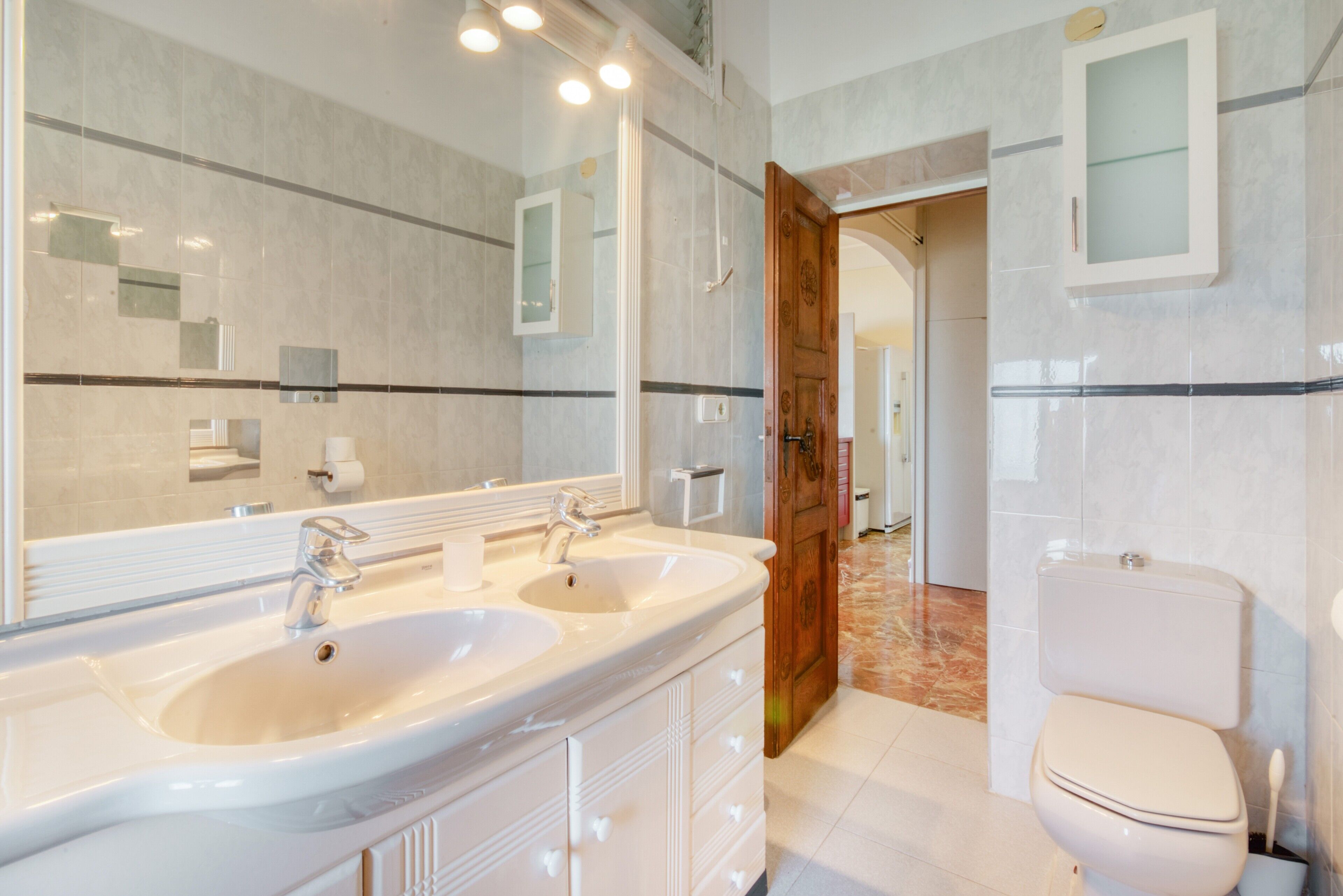 Une salle de bain avec deux lavabos, un miroir, des toilettes et une porte en bois.