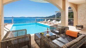 Un área junto a la piscina con muebles de mimbre, una mesa con una botella y vasos, y vistas al mar.