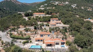 Uma propriedade em encosta com vários edifícios, piscina e estrada serpenteando pela área.