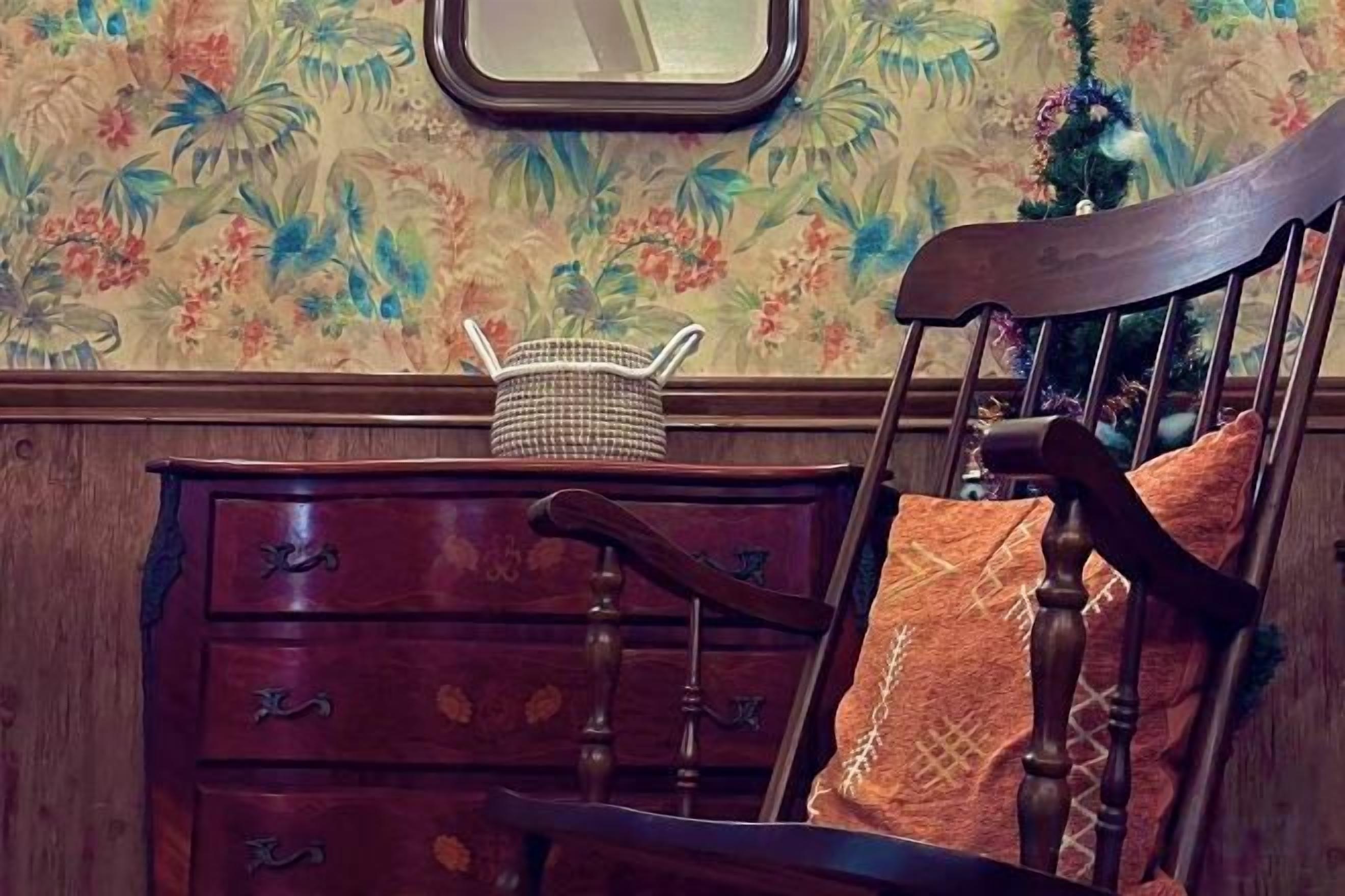 A wooden dresser with drawers, a wicker basket, and a chair with a patterned cushion.