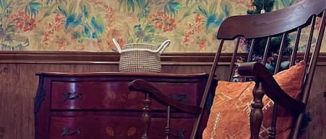A wooden dresser with drawers, a wicker basket, and a chair with a patterned cushion.