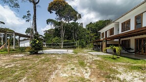 Un patio con una red de voleibol, rodeado de árboles y un edificio con ventanales grandes.