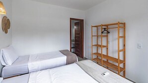 Una habitación con dos camas individuales, una estantería de madera y una puerta que da a un armario.