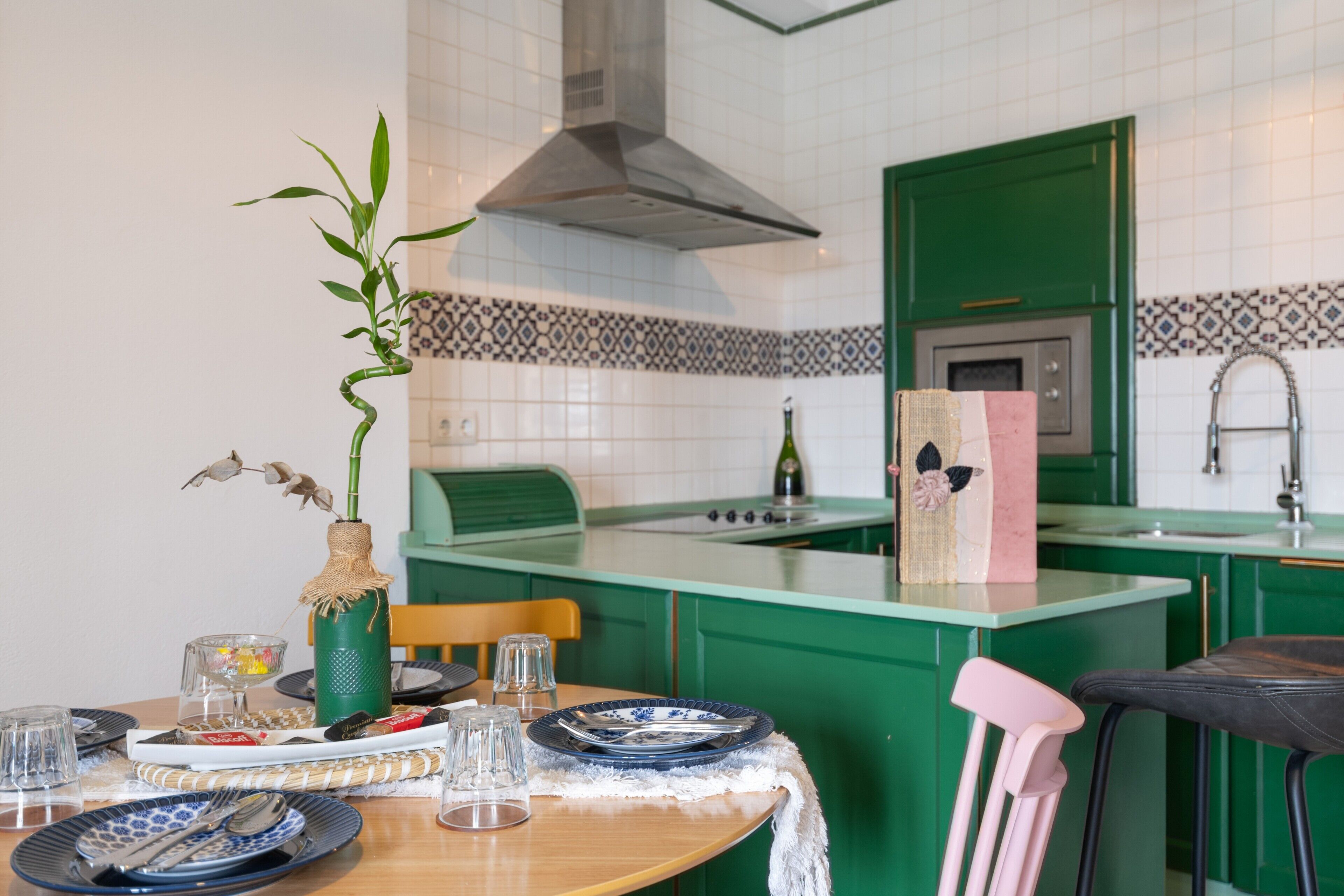 Ett kök med gröna skåp, en köksö och ett matbord som är dukat med tallrikar och glas.