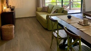 Ein Zimmer mit einer Couch, einem Esstisch, Stühlen, einer Hängelampe, einem Fenster mit Vorhängen und einem Deckenventilator.