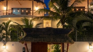 Ein Resort mit einem Reedeingang, Zimmerpflanzen und einem gut beleuchteten Gebäude im Hintergrund.