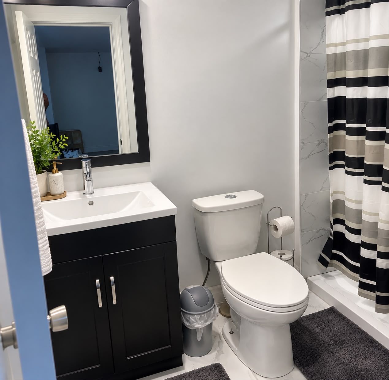 A modern bathroom with a white sink, black cabinets, a toilet, and a striped shower curtain.