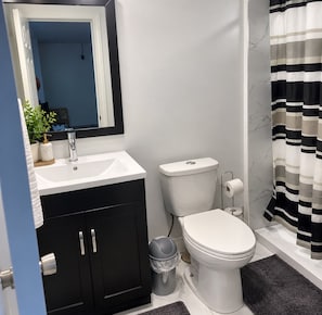 A modern bathroom with a white sink, black cabinets, a toilet, and a striped shower curtain.