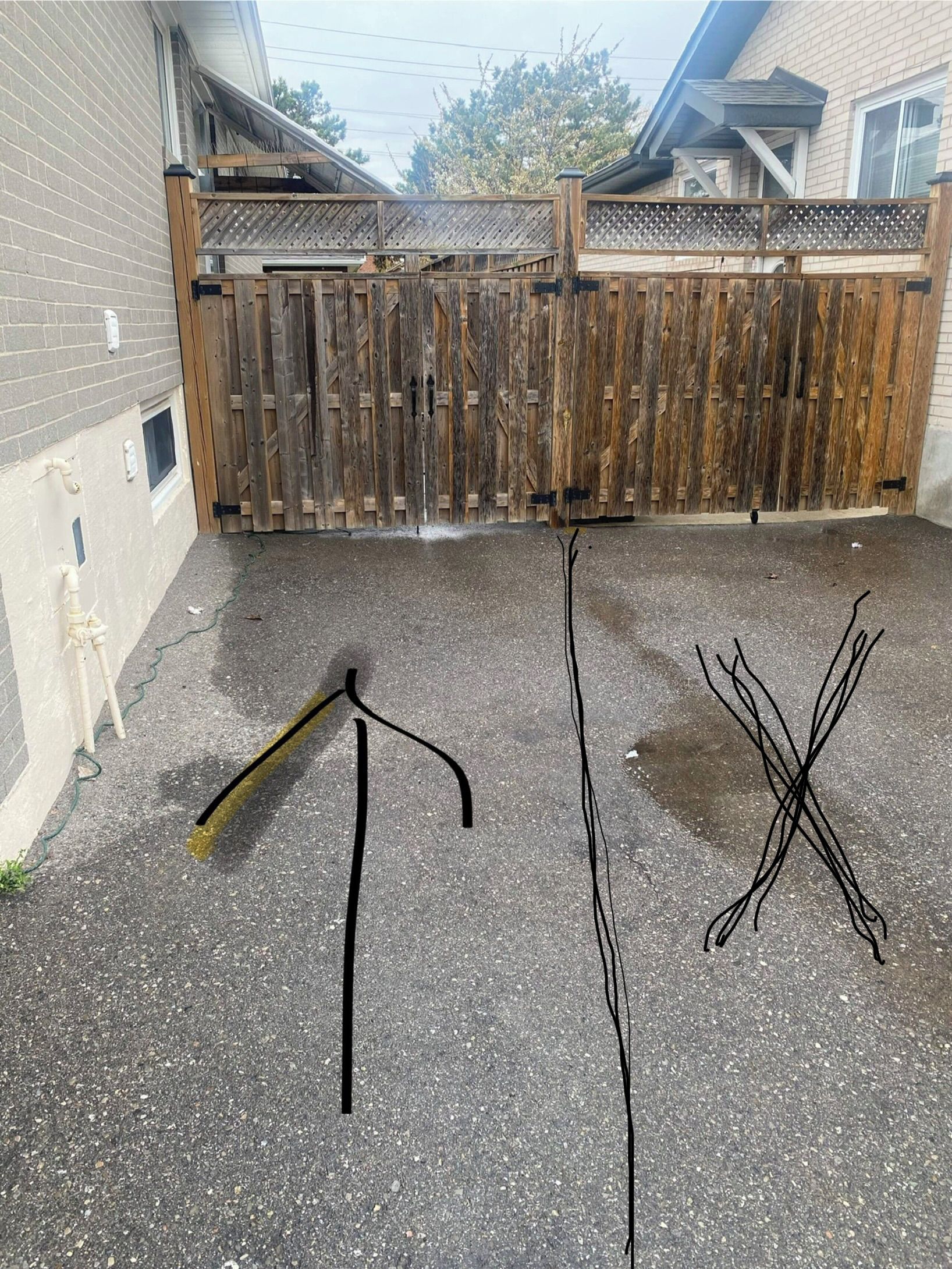 Une zone extérieure dallée, entourée d’une clôture en bois, avec un trépied et deux poteaux noirs.