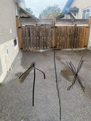 A paved outdoor area with a wooden fence, a tripod, and two black poles. - Basement studio in Mississauga (Mississauga)