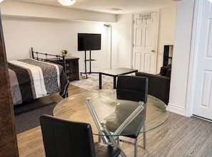A room with a bed, a glass table with chairs, a TV, and a door.