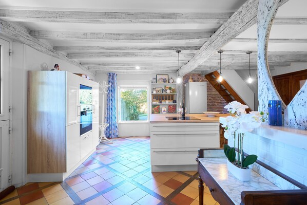 Une cuisine avec des meubles blancs, un banc en bois et une orchidée en pot.