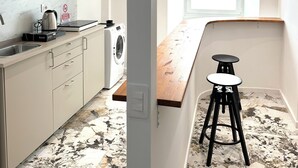 A modern kitchen with a built-in oven, microwave, and washing machine. There is a wooden countertop and two black stools. The floor has a marble-like pattern. - Callas Luxury Apartment (Roma)