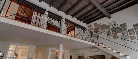 A spacious living area with a staircase, wooden ceiling, and a television on a wooden stand.