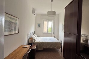 Een slaapkamer met een bed, een bureau, een stoel, een hanglamp en een kledingkast.