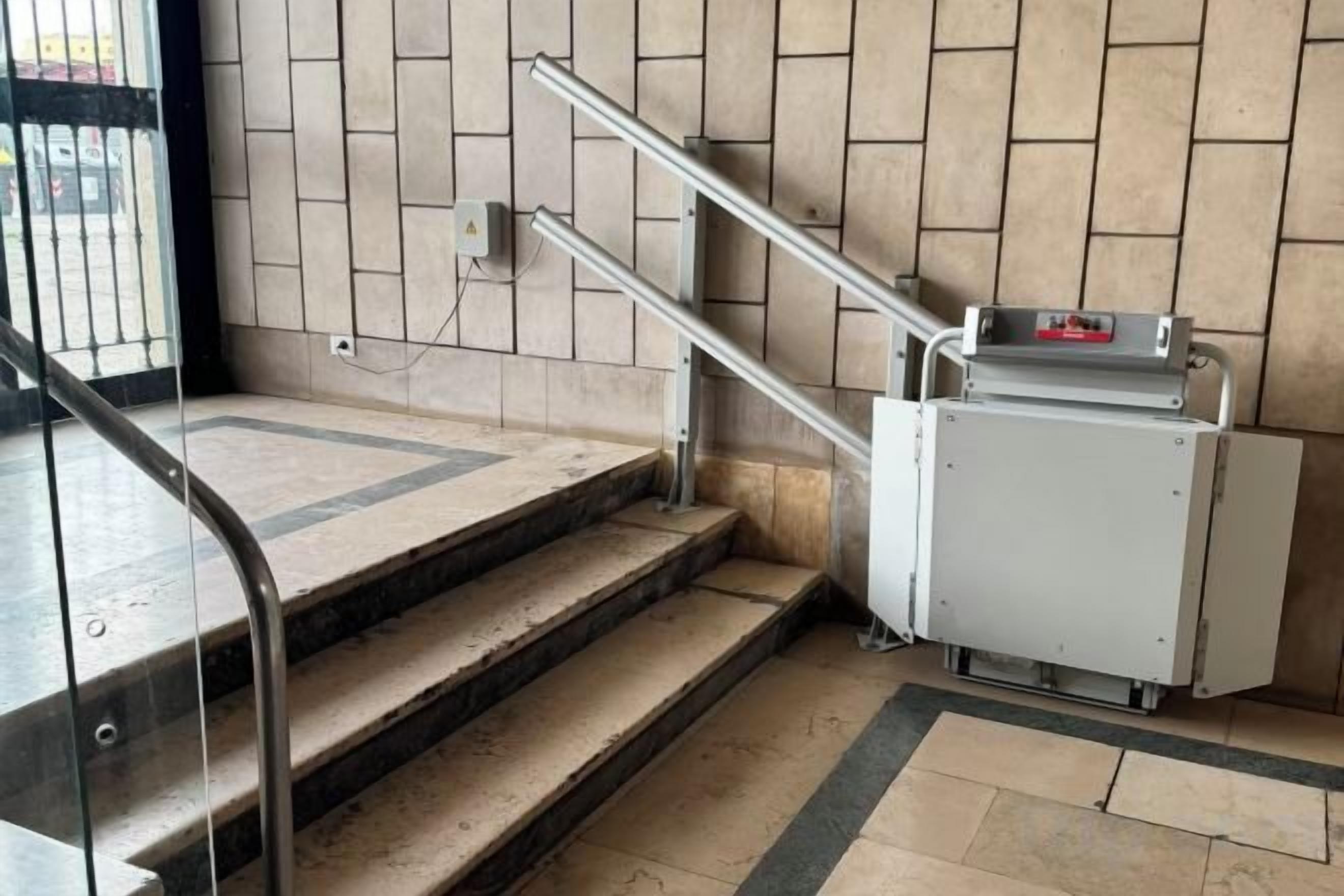 A staircase with metal handrails, a tiled wall, and a small electrical box on the floor.