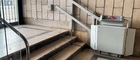 A staircase with metal handrails, a tiled wall, and a small electrical box on the floor.