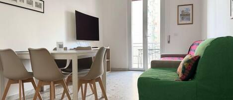 A room with a dining table, chairs, a green sofa, a TV, and a door leading to a balcony.