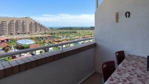 Un balcón con mesa y sillas, vista a una zona residencial y cielo despejado.