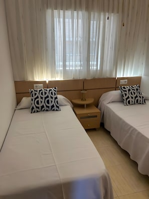 Una habitación de hotel con dos camas, una mesita de noche, una lámpara y una ventana con cortinas.