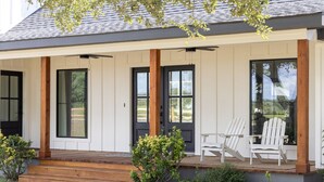 Una casa moderna con un porche cubierto, dos sillas Adirondack blancas y un pequeño jardín.