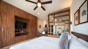 A bedroom with a large bed, wooden wardrobe, TV, and a built-in shelving unit. - 1 Bedroom Pool & Gym Bahay 504 (Playa del Carmen)