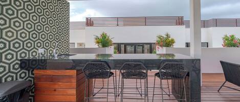 Un patio al aire libre con zona de bar, que incluye una barra de madera y sillas de metal.