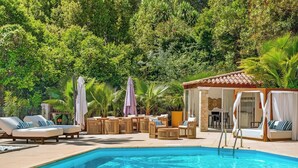 Un espace piscine avec des chaises longues, une terrasse en bois et un coin salon abrité.