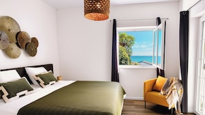 Une chambre avec un lit, une chaise, une fenêtre donnant sur un beau paysage et un luminaire suspendu.