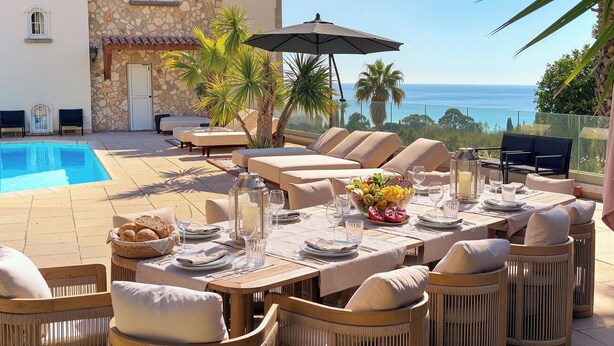 Un espace de restauration situé au bord de la piscine, avec des sièges en plein air, une table dressée pour un repas et une vue sur l’océan.