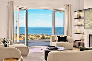 A modern living room with a large sliding glass door leading to a balcony with a city and ocean view. - Villa Roc d’Azur, Heated Pool all year & Jacuzzi (Vallauris)