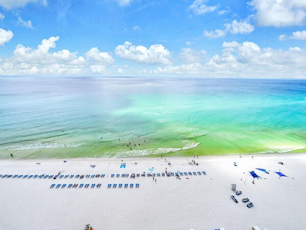 A beach with clear turquoise water, white sand, and a row of blue sun loungers.