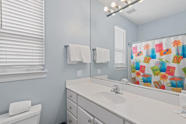A bathroom with a white sink, a mirror, and a shower curtain with a tropical design. - Destiny Beach Villas #23a&b- Beachy Keen (Destin)