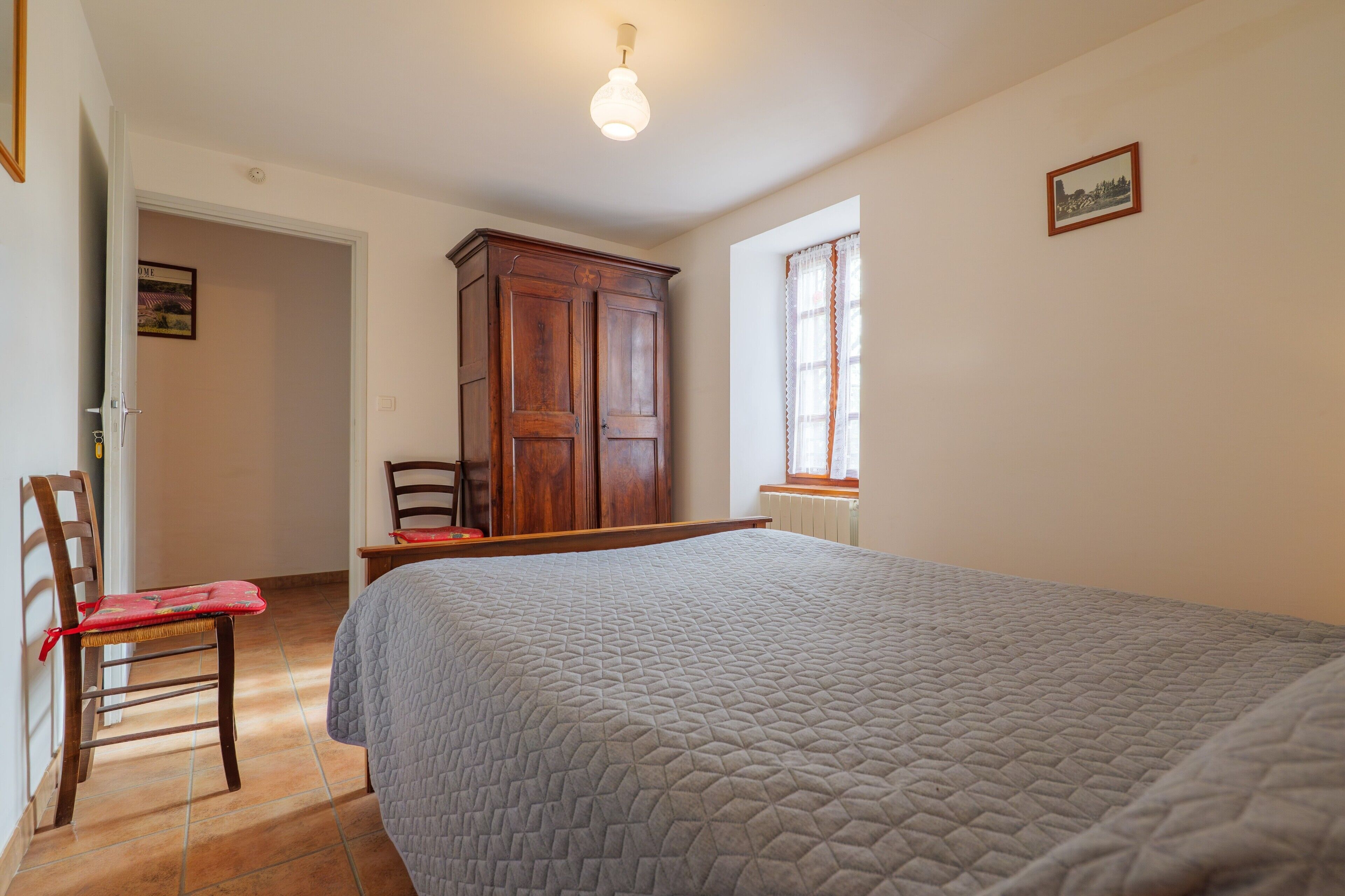 Een slaapkamer met een bed, een houten garderobe, een stoel en een raam.