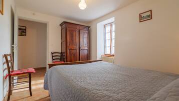 Een slaapkamer met een bed, een houten garderobe, een stoel en een raam.