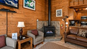 Una sala de estar acogedora con chimenea, paredes de madera, un sofá, un sillón y una mesa de centro.