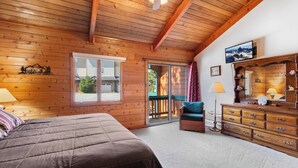 Una habitación acogedora con techo de madera, una cama, una silla, un aparador y un televisor.