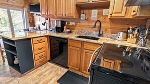Una cocina con armarios de madera, encimera de granito, lavavajillas, estufa y pileta.