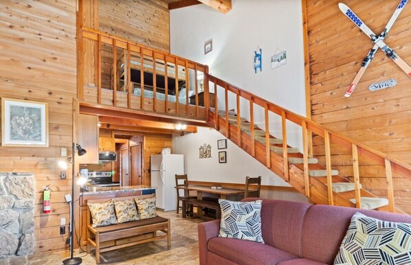 A wooden interior with a staircase, a dining area, and a sofa with patterned cushions. - The Pacesetter Best Location on the Mountain (Snowshoe)