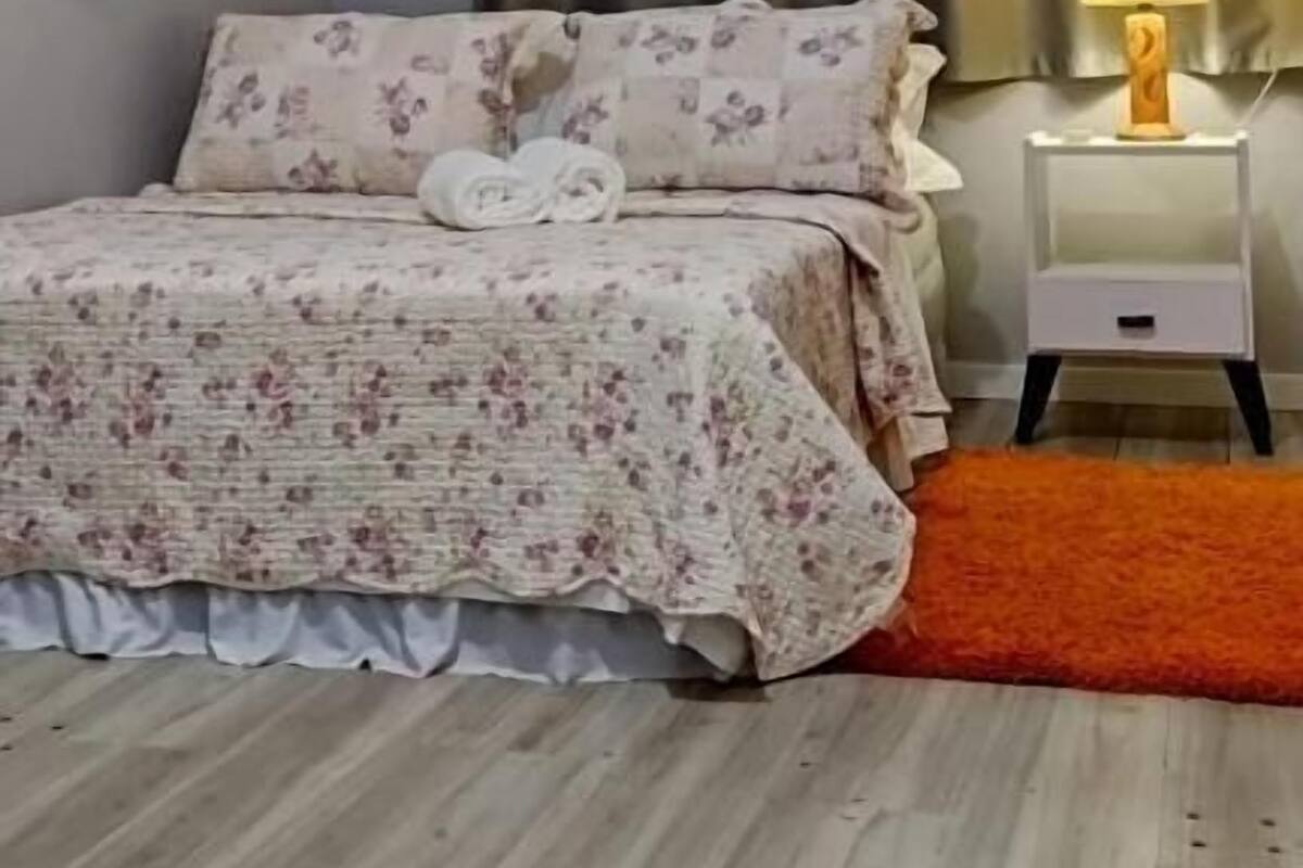 Une chambre à coucher avec un lit, une table de chevet, une lampe et une fenêtre avec des rideaux.