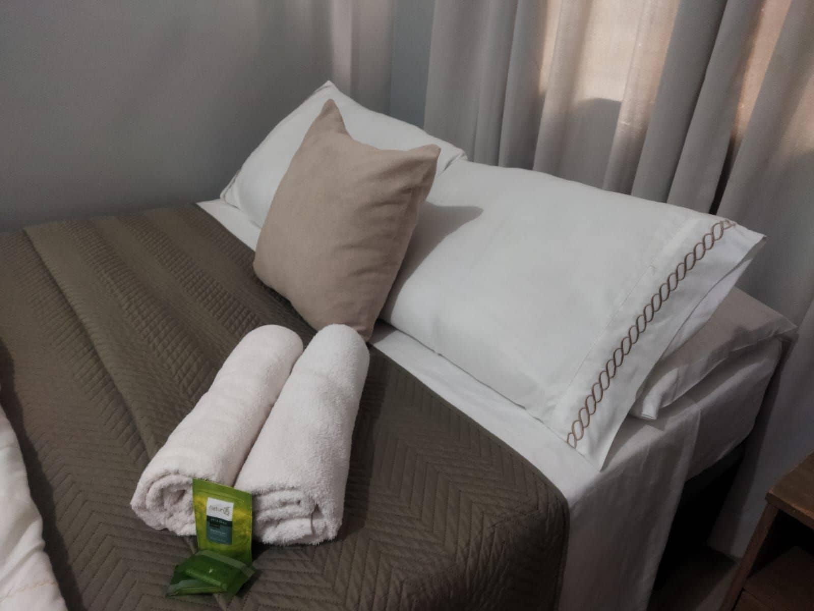 A neatly made bed with white and beige pillows, a brown bedspread, and a green item on the bed.