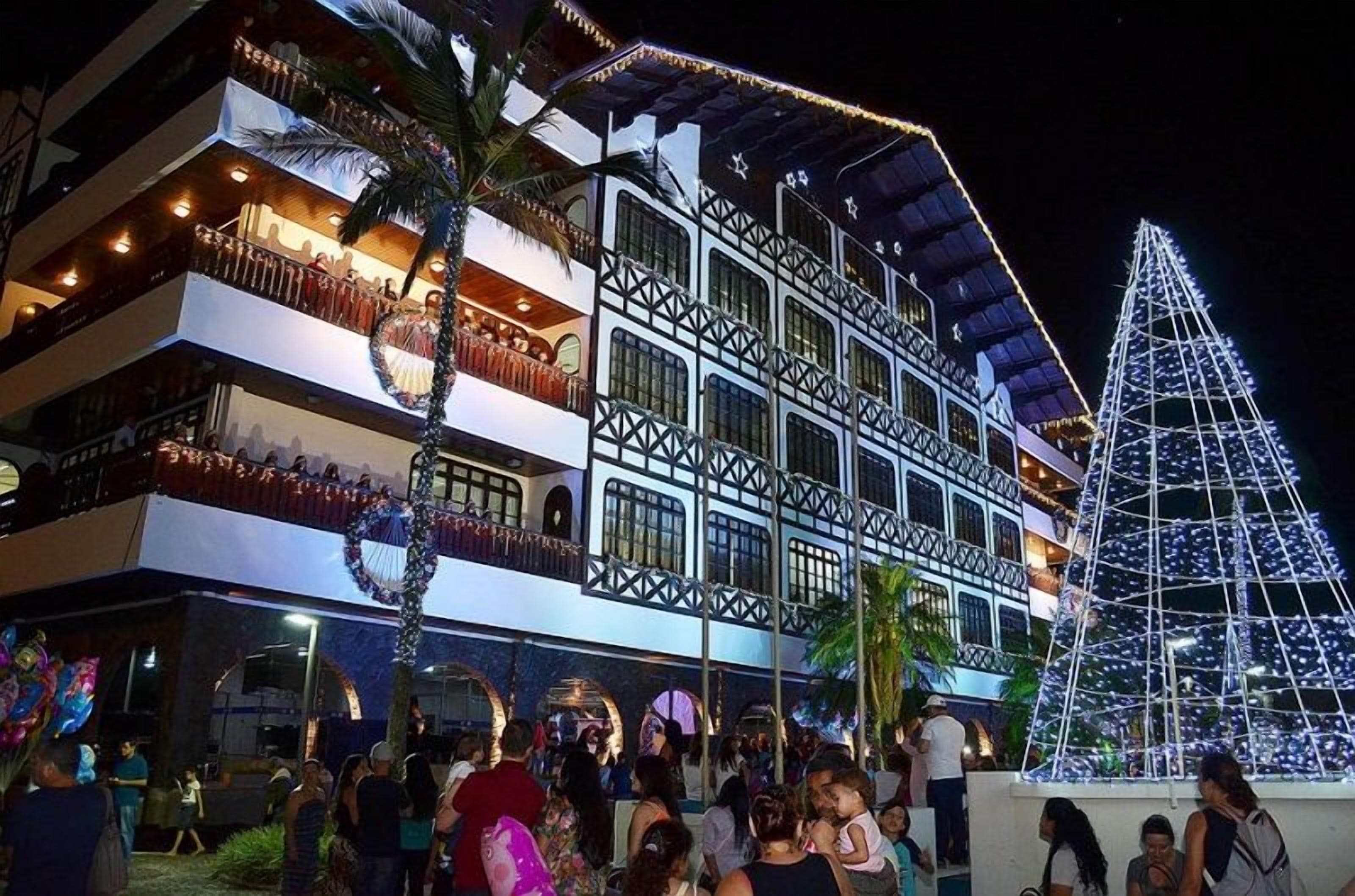 A multi-story hotel with balconies, a large Christmas tree, and a crowd of people.